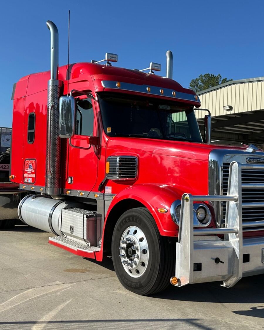 A red GTI Transport Freightliner with a loaded flatbed at an industrial plant