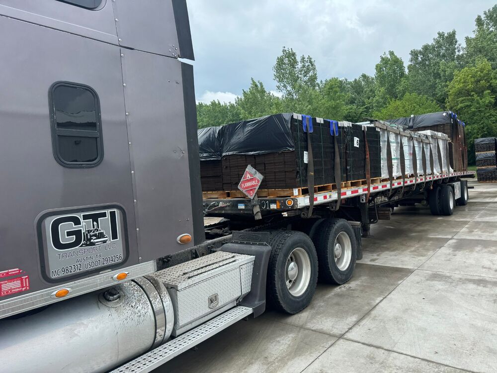 A GTI Transport Peterbilt with a tarped flatbed load and a flammable placard