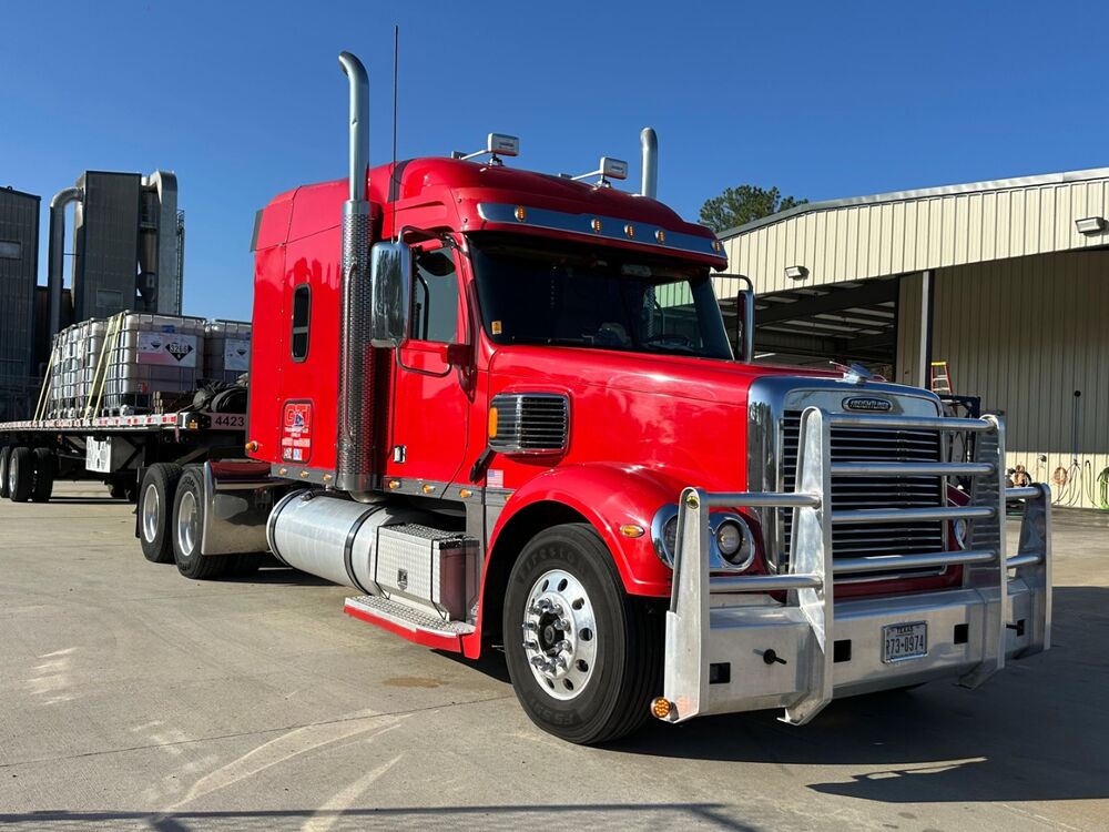 A red GTI Transport Freightliner with a loaded flatbed at an industrial plant